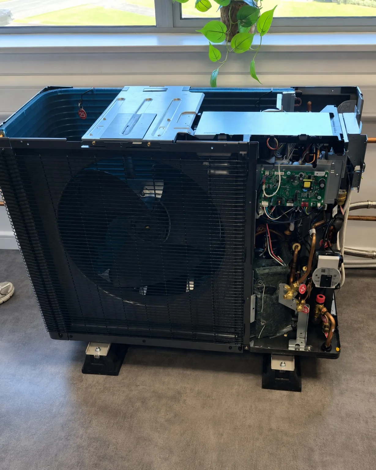 Air source heat pump outdoor unit with the casing removed, showing the fan, electronics, compressor and internal pipework